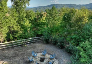 Blue Adirondack chairs by fire pit with mountain ridges in scenic Blue Ridge vacation rental backyard