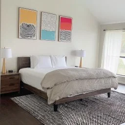 Modern minimalist bedroom with white linens, wooden nightstands, and contemporary art at The Waterfront Villa in Montgomery,