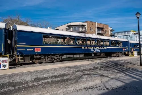 Vintage blue and gold Blue Ridge Scenic Railroad train car under a clear sky, near hiking trails and cabins with hot tubs in