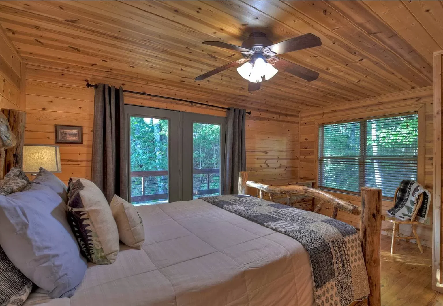 Rustic cabin bedroom with wood beams and king bed opening to forest-view deck in Blue Ridge