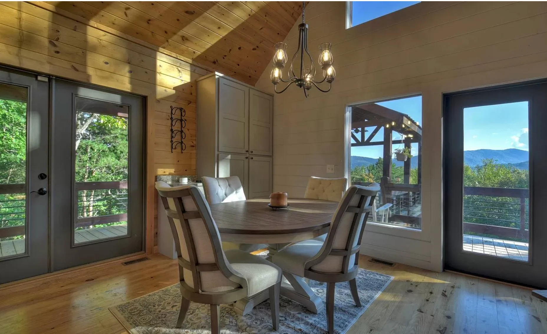 Dining room with round wood table, upholstered chairs, exposed beams and mountain views at Chalet Blue Ridge, a Nest Awaits