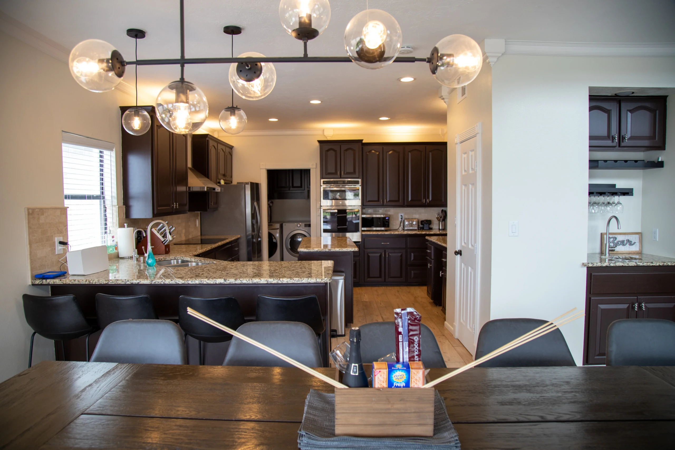 Modern open-concept kitchen with dark wood cabinets, granite counters, and a glass globe pendant light over a breakfast bar