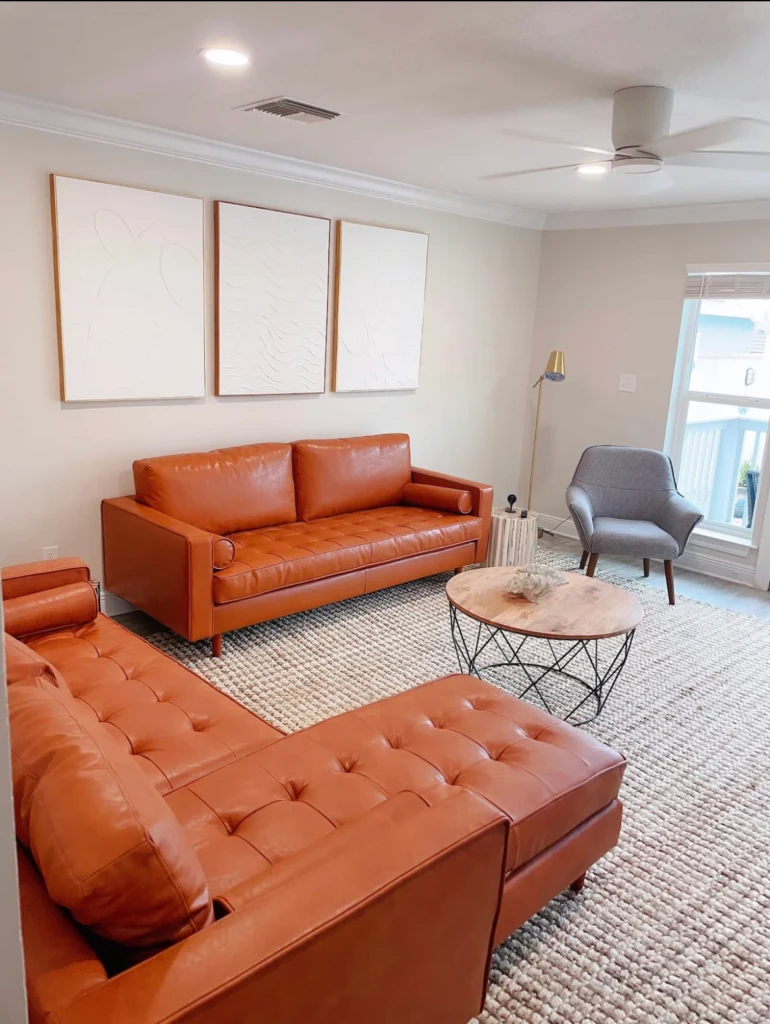 Modern living room with burnt orange leather sofa and grey accent chair near sliding glass doors with ocean view, a best