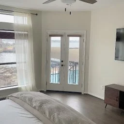 Bright master bedroom with French doors, white sheer curtains, and waterfront views in The Waterfront Villa, Montgomery TX