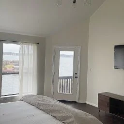 Bright bedroom with white curtains, wooden nightstand, and waterfront views through sliding glass doors, a family comparing
