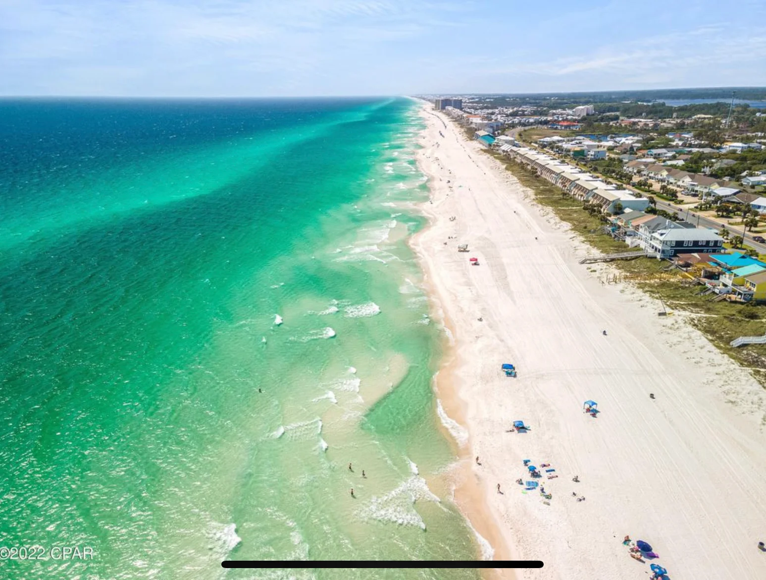 Aerial view of turquoise coastal waters, white sand beach, and beachfront homes with a blue pool in Panama City Beach, FL